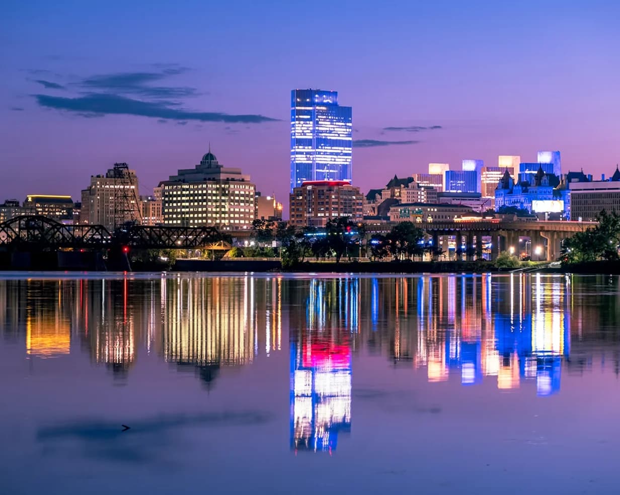 Downtown Albany, New York skyline reflected in the Hudson River at twilight, a staging point for charter bus groups