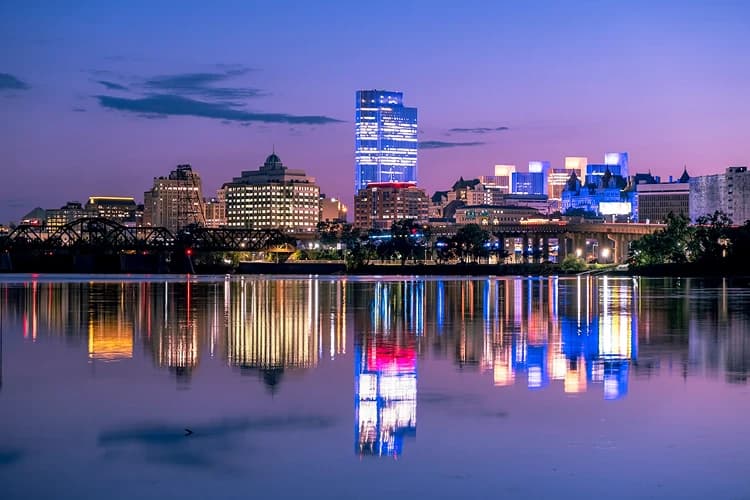 Downtown Albany, New York skyline reflected in the Hudson River at twilight, a staging point for charter bus groups