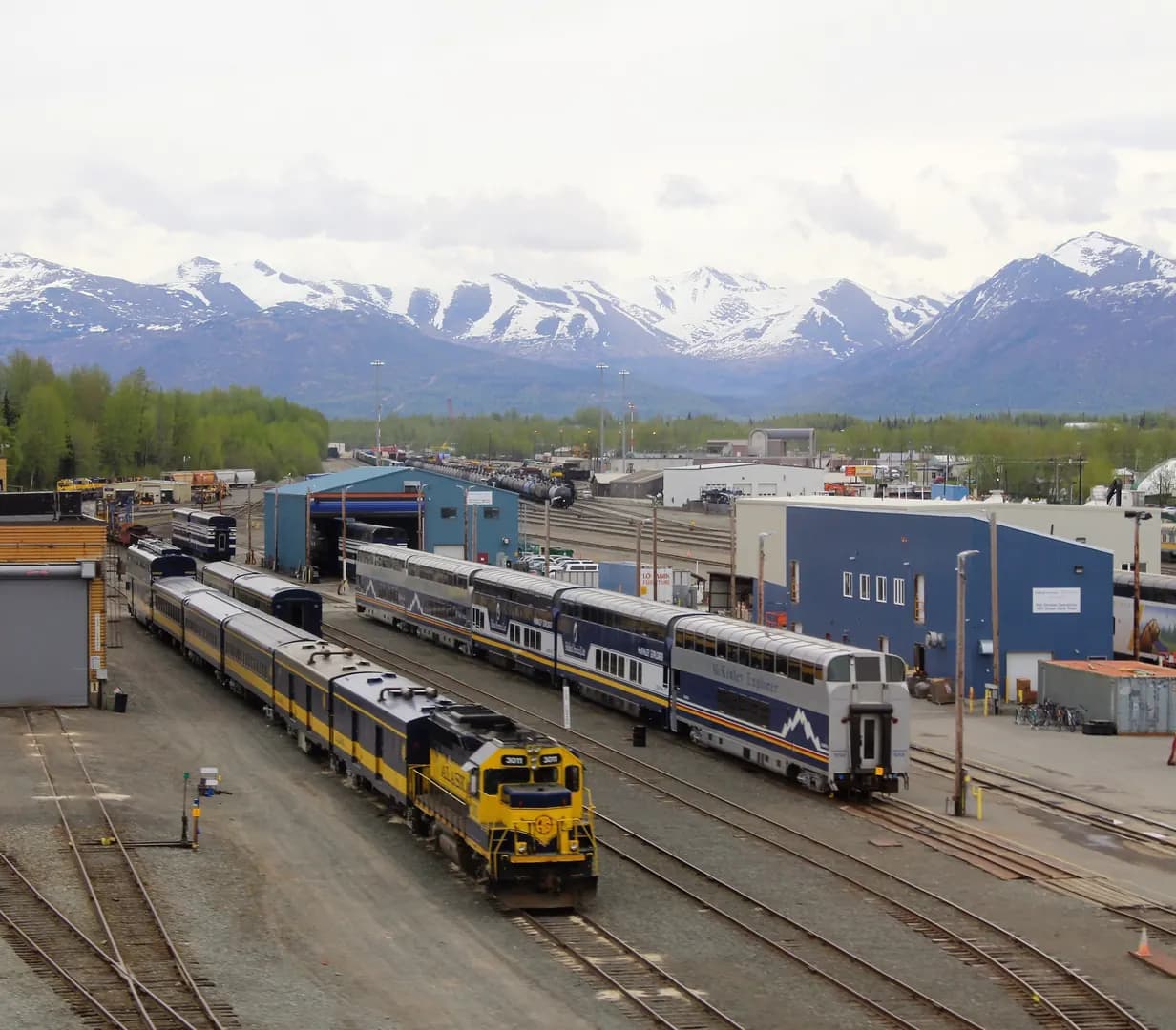 Alaska Railroad trains, including the McKinley Explorer, in the Anchorage rail yard below the snow-capped Chugach Mountains