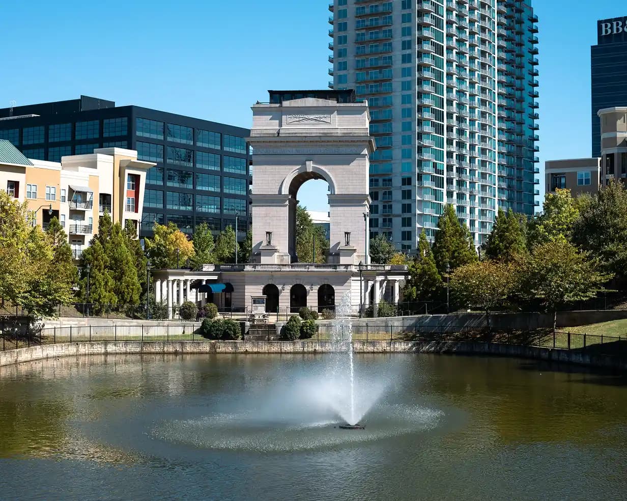 Millennium Gate triumphal arch and reflecting pond in Atlanta, Georgia with the skyline behind it, near Atlantic Station charter bus pickups