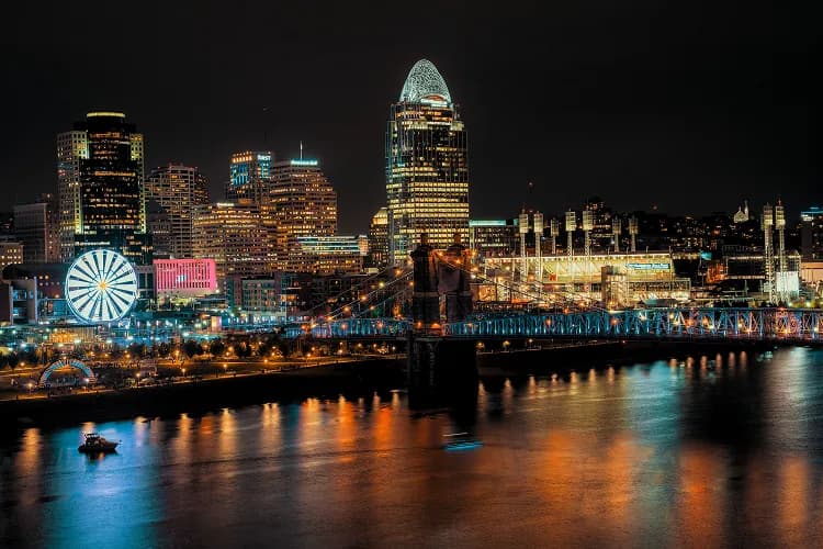 Downtown Cincinnati, Ohio skyline at night with the Roebling Suspension Bridge and riverfront Ferris wheel, where charter bus groups board for Reds and Bengals games