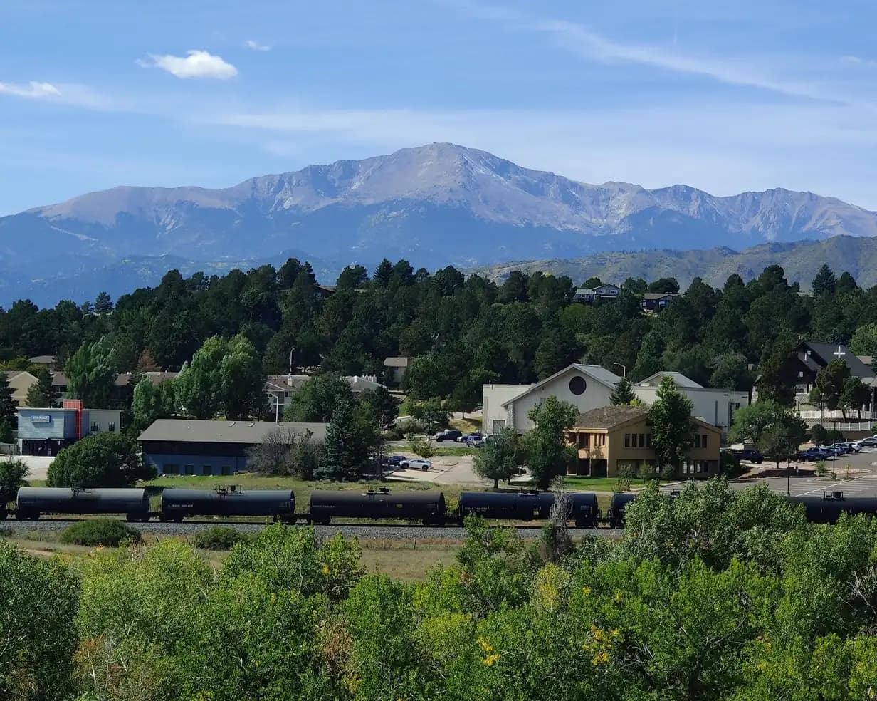 Pikes Peak rising above pine trees, buildings and a passing freight train in Colorado Springs, Colorado