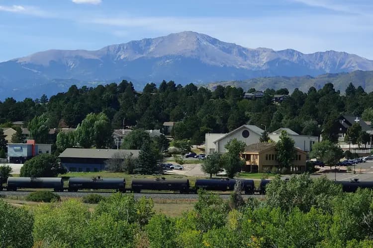 Pikes Peak rising above pine trees, buildings and a passing freight train in Colorado Springs, Colorado