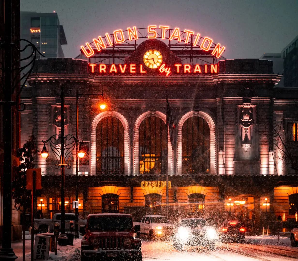 Neon Union Station Travel by Train sign glowing above the station entrance on a snowy night in downtown Denver, Colorado