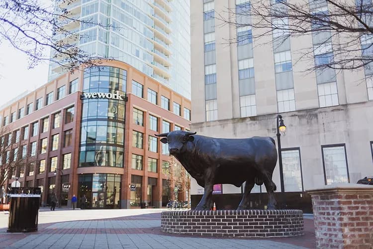 Bronze bull statue in downtown Durham, North Carolina, the "Bull City" landmark beside the modern skyline where charter bus groups stage