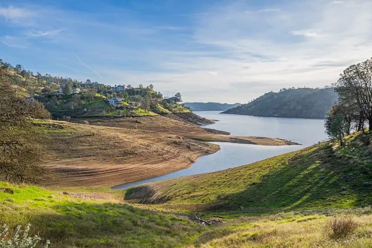 Winding reservoir between green foothills, with homes on the slopes, at Millerton Lake near Fresno, California