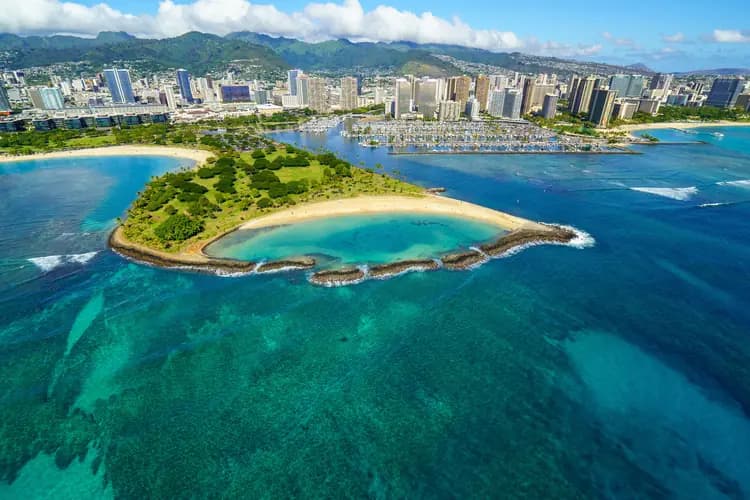 Aerial view of the Magic Island lagoon at Ala Moana Beach Park with the Waikiki skyline and mountains in Honolulu, Hawaii