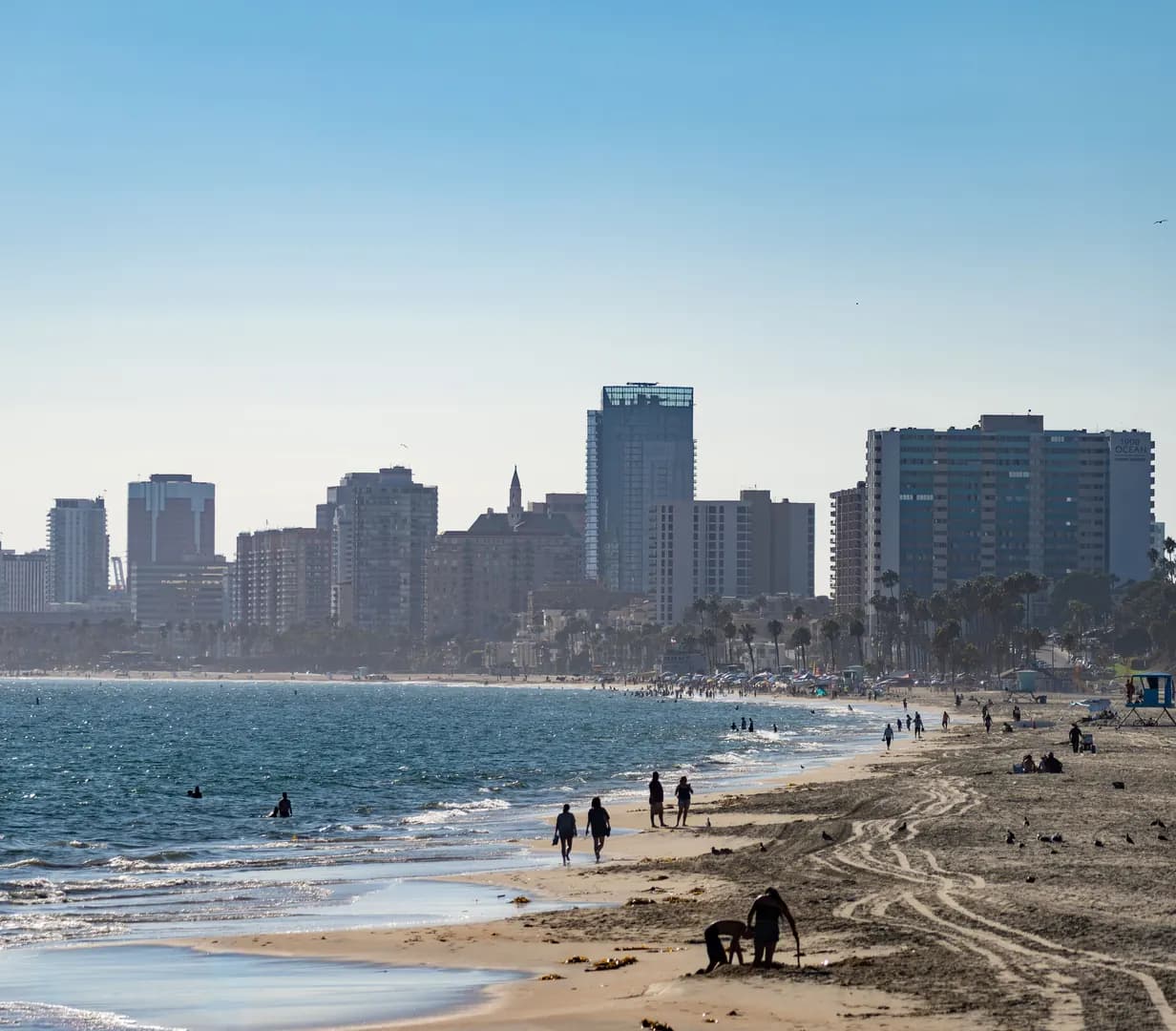 Beachgoers on the sand with the downtown Long Beach, California skyline along the shoreline on a sunny day