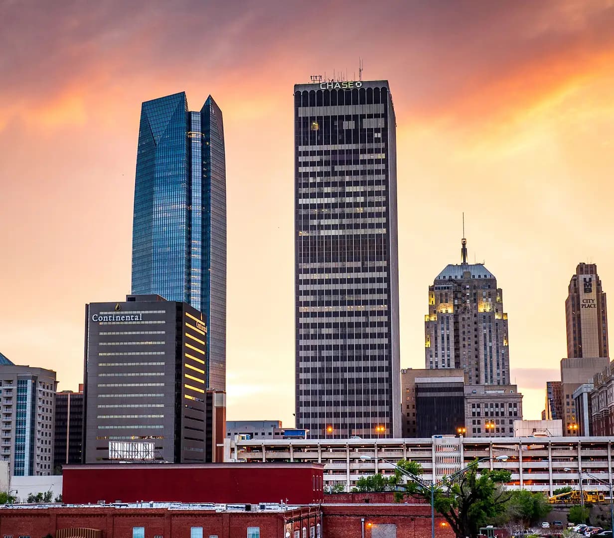 Downtown Oklahoma City, Oklahoma skyline skyscrapers against an orange sunset sky, a charter bus pickup area