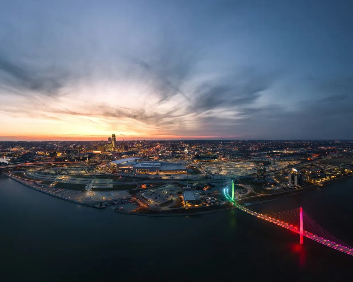 Aerial view of the Omaha, Nebraska skyline at sunset, with the lit Bob Kerrey Pedestrian Bridge over the Missouri River