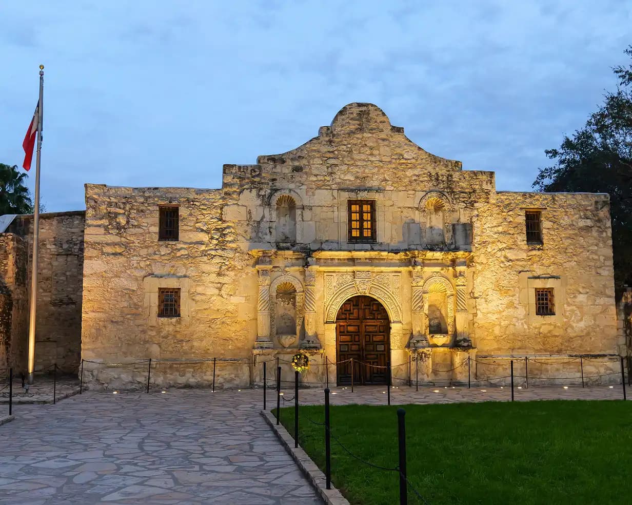 The Alamo mission stone facade lit at dusk in San Antonio, Texas, a charter bus downtown tour stop