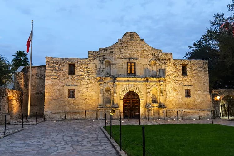 The Alamo mission stone facade lit at dusk in San Antonio, Texas, a charter bus downtown tour stop