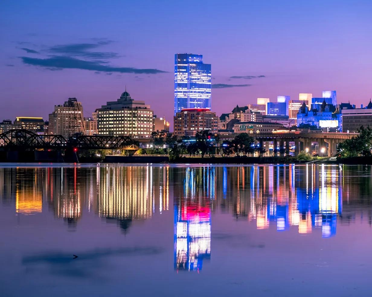 Downtown Albany, New York skyline reflected in the Hudson River at twilight, a staging point for charter bus groups