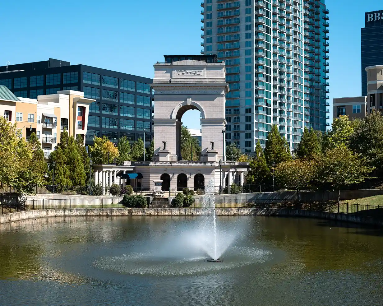 Millennium Gate triumphal arch and reflecting pond in Atlanta, Georgia with the skyline behind it, near Atlantic Station charter bus pickups