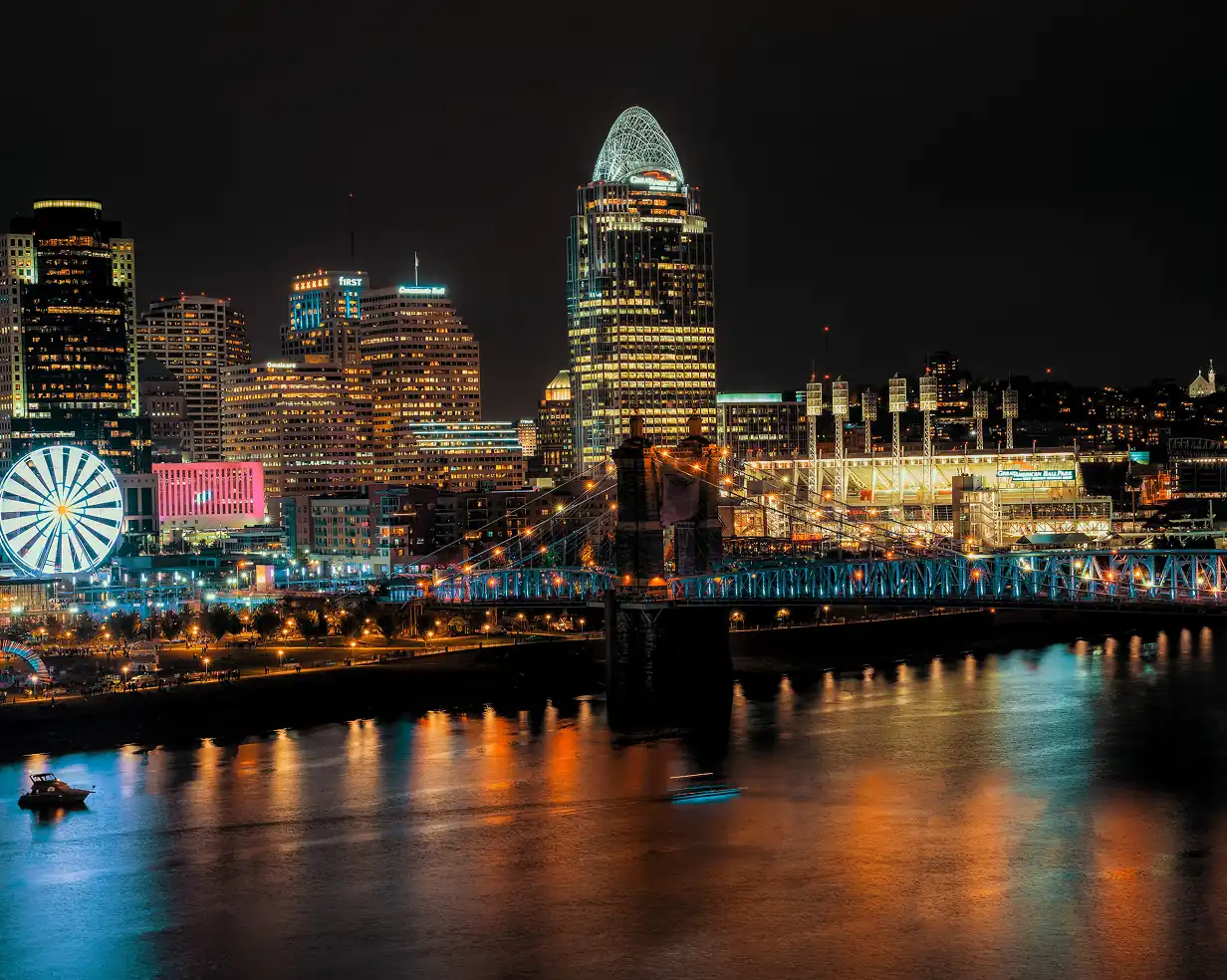 Downtown Cincinnati, Ohio skyline at night with the Roebling Suspension Bridge and riverfront Ferris wheel, where charter bus groups board for Reds and Bengals games