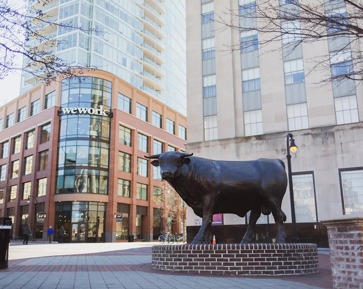 Bronze bull statue in downtown Durham, North Carolina, the "Bull City" landmark beside the modern skyline where charter bus groups stage