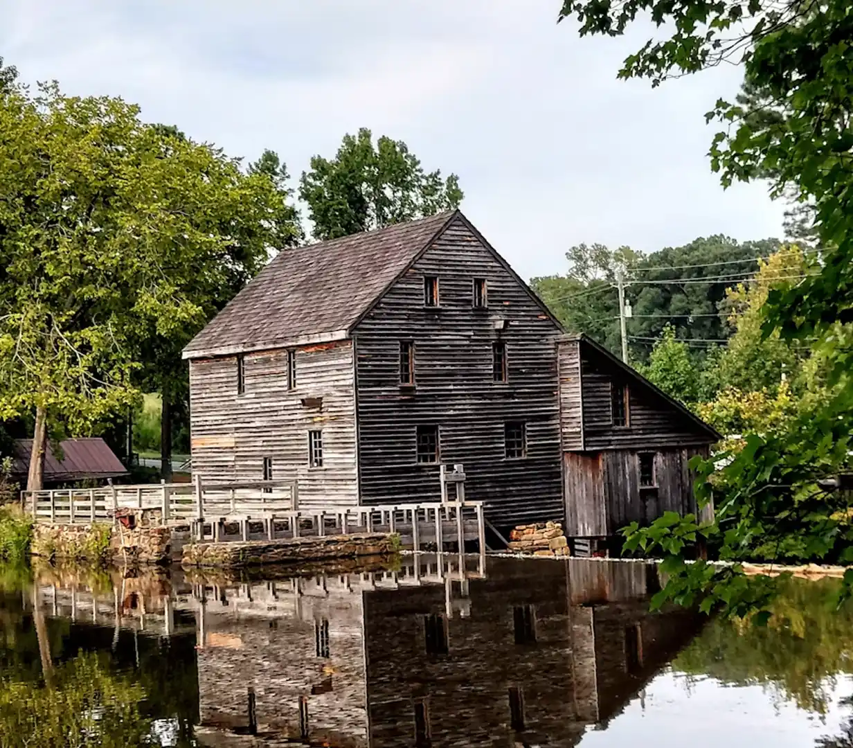 Historic wooden grist mill reflected in the pond at Yates Mill County Park in Raleigh, North Carolina, a field-trip stop for charter bus groups